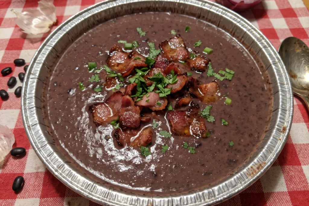 Caldinho de feijão com bacon cremoso servido em tigela, com bacon crocante, cheiro-verde e torradinhas