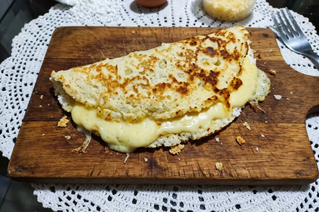 Crepioca de queijo douradinha na frigideira, recheada com queijo derretido e pronta para o café da manhã.