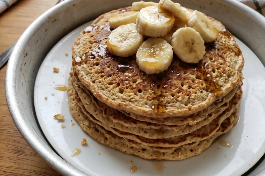 Panqueca de aveia com banana fofinha e dourada, servida com rodelas de banana, canela e um fio de mel